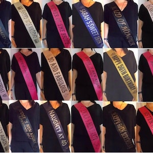 May include: Collection of sashes in various colors, each with celebratory text. Sashes include phrases like "Bridesmaid," "Happy 18th Birthday," and "Mother of the Bride." The sashes are worn over black tops, with text in gold, silver, and white.