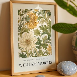 Op de afbeelding: Een ingelijste kunstprint met een bloemmotief in geel, crème en groen. De print bevat de tekst "ART NOUVEAU . MOTIF CLASSIQUE" en "WILLIAM MORRIS". De lijst is van lichtkleurig hout.
