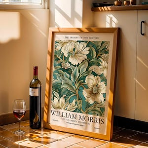 Può includere: Una stampa incorniciata con un motivo floreale color crema e verde, appoggiata a un muro. Una bottiglia di vino rosso e un bicchiere da vino sono davanti alla stampa. La stampa presenta il testo "WILLIAM MORRIS".