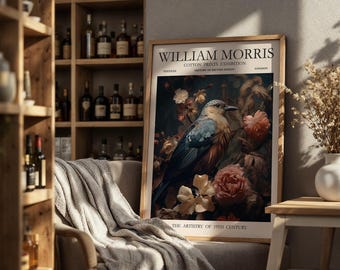 May include: A framed print featuring a detailed illustration of a bird amidst flowers. The print is labeled "William Morris Cotton Prints Exhibition" with text about the history of British design. The artwork is displayed in a room with a wooden bookshelf and a cozy chair.