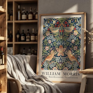 Op de afbeelding: Een ingelijste kunstdruk met een William Morris-ontwerp, met vogels en bloemmotieven in blauwe, groene en roze tinten. De print bevat de tekst "WILLIAM MORRIS" en "the Smithsonian Institution". Het kunstwerk wordt tentoongesteld in een kamer met een houten boekenplank.