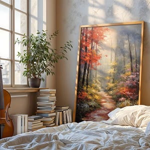 Può includere: Un dipinto di paesaggio incorniciato raffigura una scena di foresta con un sentiero, con un vivace fogliame rosso e giallo. Un violoncello si trova vicino a una finestra con una pianta in vaso e pile di libri. La scena è ambientata in una camera da letto con un letto e cuscini.