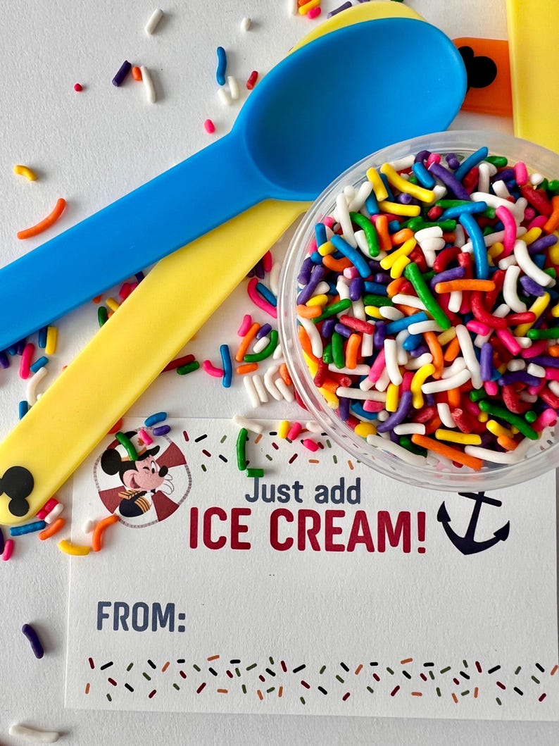 May include: A white card with a cartoon image of Mickey Mouse wearing a captain's hat. The card says "Just add ICE CREAM!" with a blue anchor symbol. The card is surrounded by colorful sprinkles and two plastic spoons, one blue and one yellow.