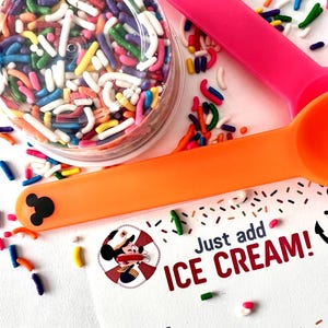 Op de afbeelding: Een witte kaart met een cartoon afbeelding van Mickey Mouse die een matrozenhoed en een reddingsboei draagt. De kaart zegt "Just add ICE CREAM!" en "FROM:"  De kaart is omringd door kleurrijke sprinkels en een kleine doorzichtige container gevuld met sprinkels. Er liggen twee oranje en roze lepels op de kaart.