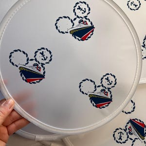 Peut inclure: Quatre éventails ronds blancs avec un motif de bateau bleu et rouge au centre. Le bateau est entouré d'un motif de corde en forme de tête de Mickey Mouse. Chaque éventail a un symbole d'ancre au-dessus du bateau.