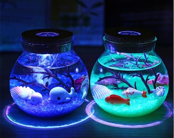 May include: Two glass jars with a blue and green glow, filled with water, small plastic fish, and seashells. The jars are on a wooden surface with a light blue and green glow underneath.
