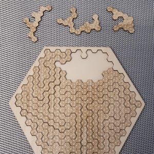Può includere: Un puzzle esagonale in legno con un motivo a nido d'ape. Al puzzle mancano alcuni pezzi, che sono mostrati separatamente.