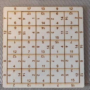 Può includere: Un tabellone di gioco in legno con una griglia di numeri. I numeri sono disposti in modo casuale. Il tabellone è in legno marrone chiaro e ha una finitura liscia.