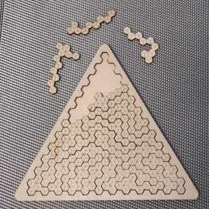 Può includere: Un puzzle di legno a forma di triangolo con un motivo geometrico di esagoni. Il puzzle è composto da pezzi esagonali più piccoli che si incastrano per creare la forma del triangolo più grande.