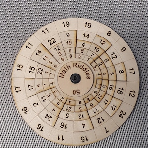 Può includere: Un puzzle circolare in legno con un quadrante rotante. Il quadrante ha numeri da 1 a 24 attorno al bordo e il testo "Math Riddles" al centro. Il puzzle è progettato per risolvere problemi di matematica.