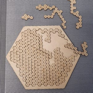 Può includere: Un puzzle esagonale in legno con un motivo geometrico di piccoli quadrati. Il puzzle è composto da molti piccoli pezzi che si incastrano per creare il disegno più grande. Al puzzle mancano alcuni pezzi, che sono mostrati separatamente.