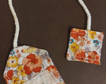 May include: Floral tea bag tags with a white cord. The tags are rectangular and feature a colorful pattern of orange, yellow, and blue flowers on a white background. The word "tea" is printed on a white label.