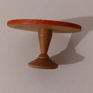 May include: A small wooden table with a round top painted orange. The table has a single, round, wooden pedestal base.