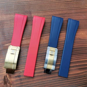 Pode incluir: Quatro pulseiras de relógio em vermelho e azul, com fechos dourados e prateados, são exibidas em uma superfície de madeira. As pulseiras são feitas de um material flexível e são projetadas para serem presas a uma caixa de relógio.