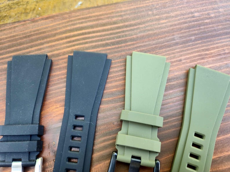 May include: Close-up of four watch straps in black and olive green. Two black straps have silver buckles and rectangular holes. The olive green straps have black buckles and rectangular holes. The straps are made of a flexible material.