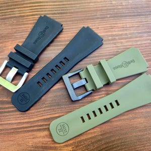 May include: Four watch straps in black and olive green, with silver and black buckles. The straps are made of a flexible material and feature the Bell & Ross logo. The straps are marked with the size 24/32 22.
