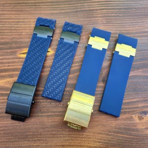 Puede incluir: Se muestran cuatro correas de reloj. Dos son de color azul marino con cierres negros y patrones texturizados. Las otras dos son de color azul marino con cierres dorados y una superficie lisa. Todas las correas están sobre una superficie de madera.