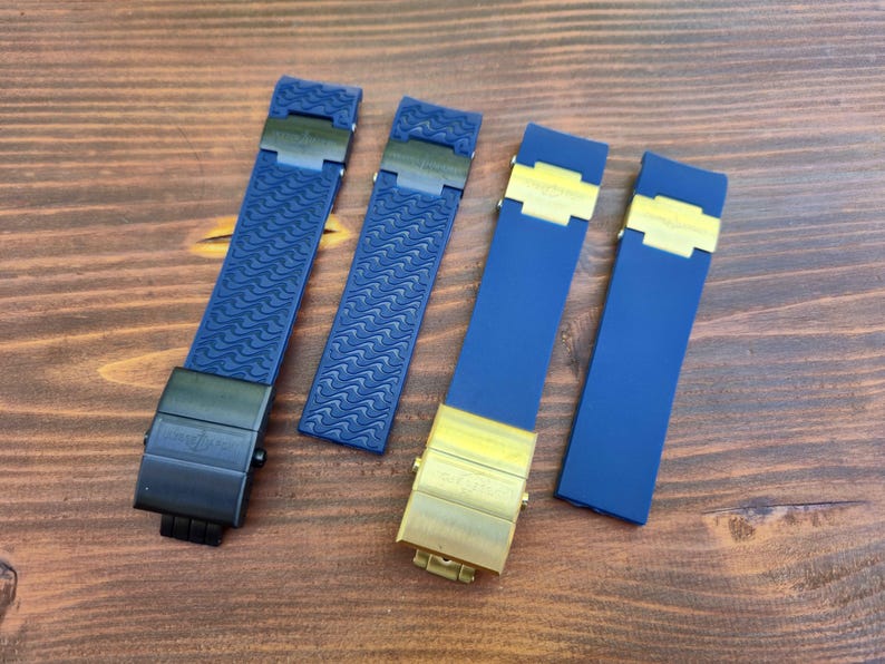 Puede incluir: Se muestran cuatro correas de reloj. Dos son de color azul marino con cierres negros y patrones texturizados. Las otras dos son de color azul marino con cierres dorados y una superficie lisa. Todas las correas est&aacute;n sobre una superficie de madera.
