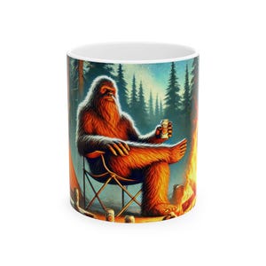 May include: White ceramic mug featuring a colorful illustration of a Bigfoot relaxing by a campfire. The Bigfoot is seated in a folding chair, holding a can of beer. The background shows a forest and a starry sky.