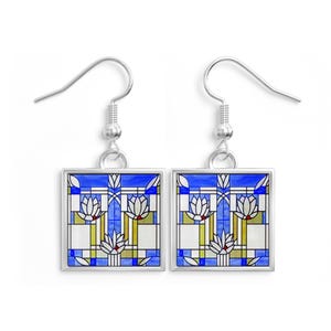 May include: A pair of silver-toned drop earrings featuring square pendants. Each pendant displays a geometric stained glass pattern in shades of blue, white, and olive green, depicting stylized floral motifs with thin black outlines.