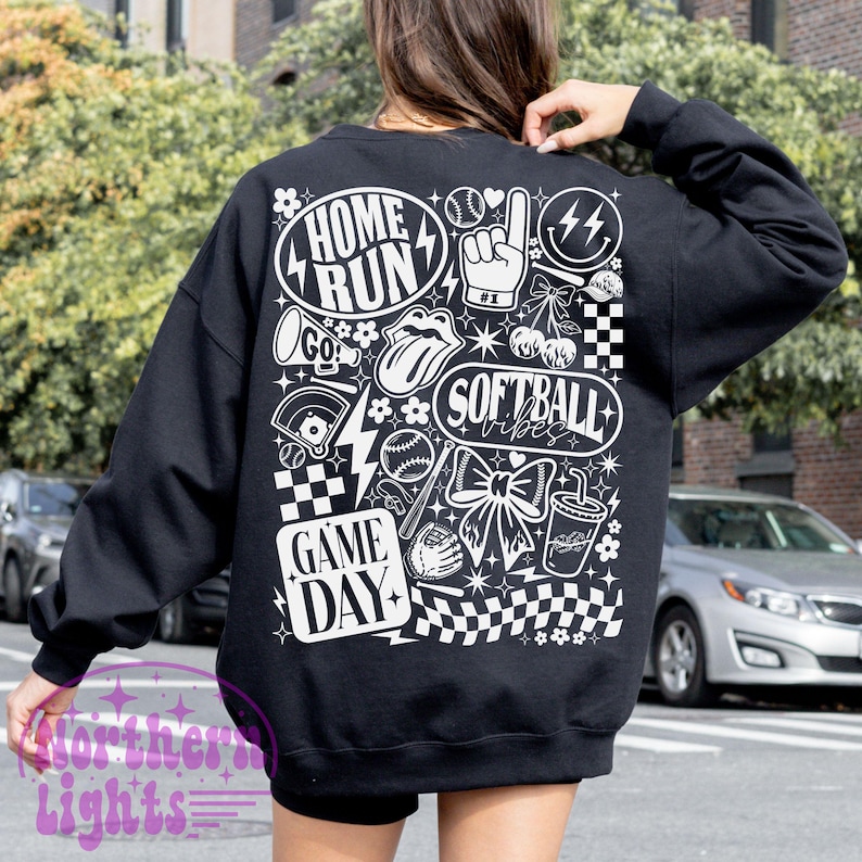 May include: Black sweatshirt with a white graphic design featuring softball-themed illustrations and text. The design includes the words "Home Run," "Softball Vibes," and "Game Day," along with baseballs, a bow, and a drink.