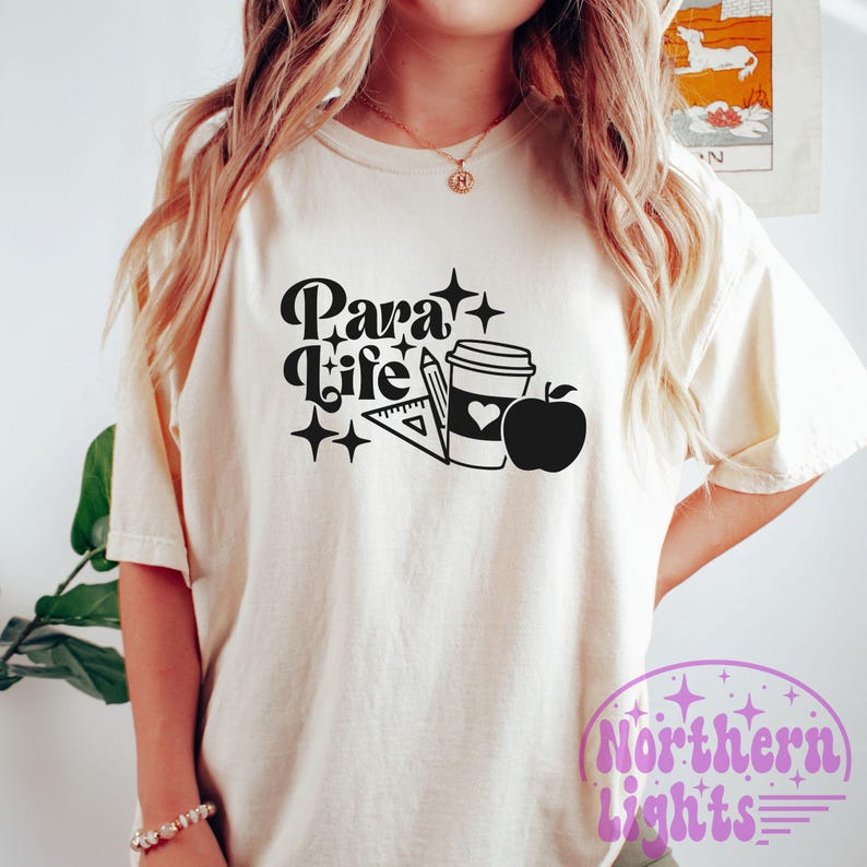 Op de afbeelding: Wit T-shirt met zwarte tekst die "Para Life" zegt en een afbeelding van een koffiebeker, een liniaal, een potlood en een appel.