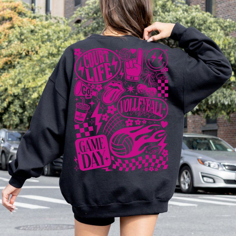 K&ouml;nnte beinhalten: Schwarzes Sweatshirt mit einem leuchtend pinkfarbenen Grafikdesign zum Thema Volleyball. Das Design enth&auml;lt die W&ouml;rter "Court Life", "Volleyball Vibes" und "Game Day". Das Sweatshirt hat einen Rundhalsausschnitt und lange &Auml;rmel.