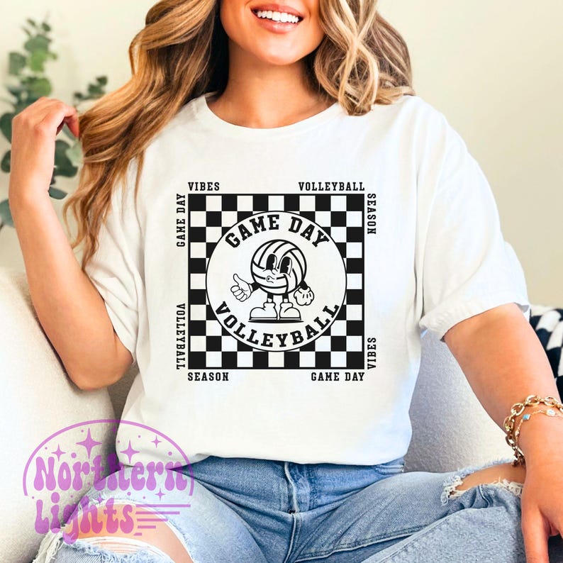 Puede incluir: Camiseta blanca con un dise&ntilde;o a cuadros blanco y negro con un bal&oacute;n de voleibol de dibujos animados con el texto "Game Day Volleyball Season Vibes" alrededor del dise&ntilde;o.