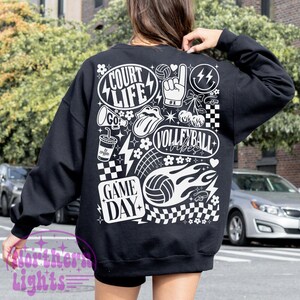 K&ouml;nnte beinhalten: Schwarzes Sweatshirt mit wei&szlig;en grafischen Designs. Das Design umfasst die W&ouml;rter "Court Life", "Volleyball Vibes" und "Game Day" sowie Volleyballb&auml;lle, Blitze und andere sportbezogene Elemente. Das Sweatshirt ist ein l&auml;ssiger Stil.