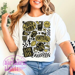 May include: White t-shirt with a football-themed graphic in black and gold. The design includes the words "Touch Down", "Football Vibes", and "Game Day", along with footballs, a helmet, and other sports-related icons.