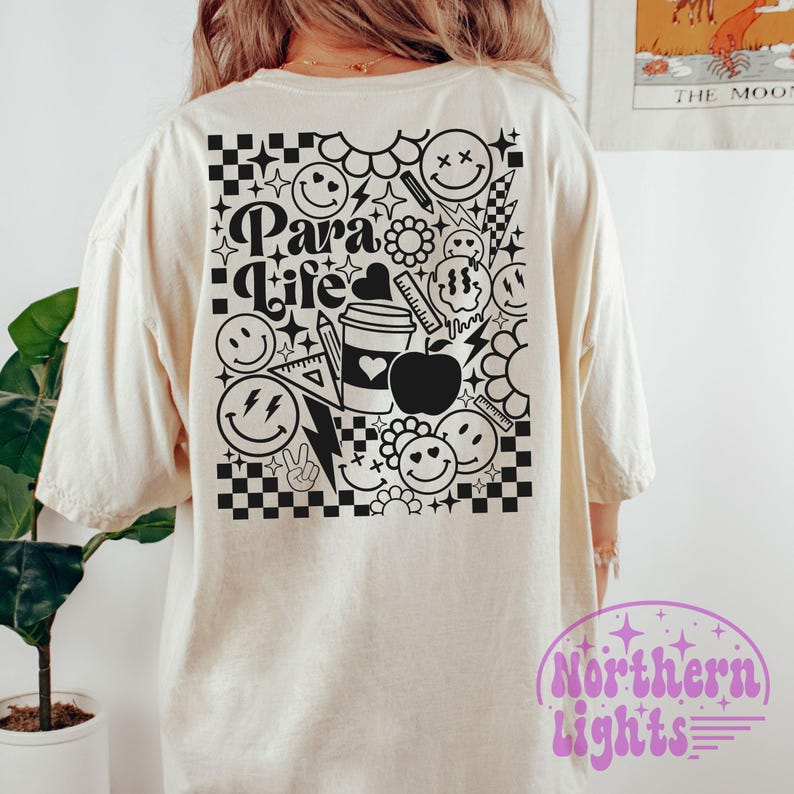 Op de afbeelding: Een wit T-shirt met een zwart grafisch ontwerp met de tekst "Para Life" omringd door smiley-gezichten, sterren en andere krabbels.