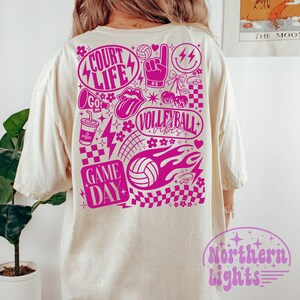 K&ouml;nnte beinhalten: Cremefarbenes T-Shirt mit einem leuchtend pinkfarbenen Grafikdesign auf der R&uuml;ckseite. Das Design enth&auml;lt die W&ouml;rter "Court Life", "Volleyball Vibes" und "Game Day" sowie Volleyb&auml;lle, Blitze und andere dekorative Elemente. Das Shirt hat eine lockere Passform.