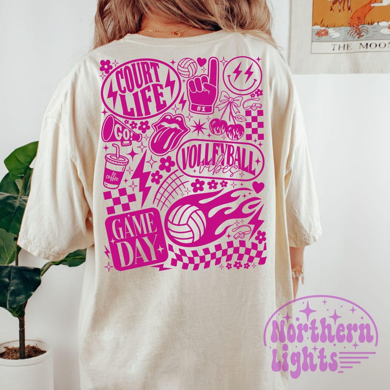 K&ouml;nnte beinhalten: Cremefarbenes T-Shirt mit einem leuchtend pinkfarbenen Grafikdesign auf der R&uuml;ckseite. Das Design enth&auml;lt die W&ouml;rter "Court Life", "Volleyball Vibes" und "Game Day" sowie Volleyb&auml;lle, Blitze und andere dekorative Elemente. Das Shirt hat eine lockere Passform.