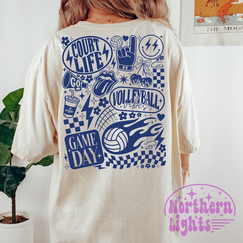 K&ouml;nnte beinhalten: Cremefarbenes T-Shirt mit einem blauen Volleyball-Motiv auf dem R&uuml;cken. Das Design enth&auml;lt die W&ouml;rter "Court Life", "Volleyball Vibes" und "Game Day" sowie Volleyballb&auml;lle, Blitze und andere sportbezogene Bilder.