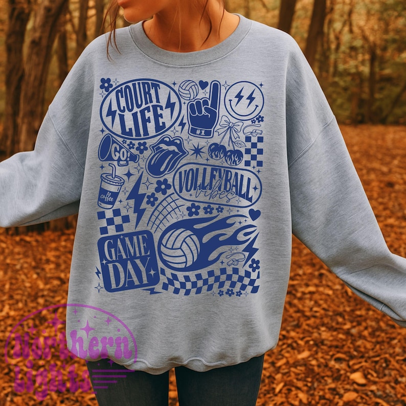 K&ouml;nnte beinhalten: Ein hellgraues Sweatshirt mit einem blauen Grafikdesign. Das Design enth&auml;lt die W&ouml;rter "Court Life", "Volleyball Vibes" und "Game Day" sowie Volleyballb&auml;lle, Blitze und andere sportbezogene Symbole.