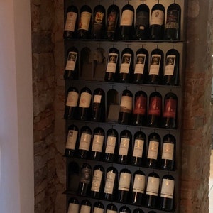 Può includere: Un porta bottiglie di vino in metallo con più file di bottiglie di vino. Il porta bottiglie è montato su un muro di mattoni. Le bottiglie sono disposte a griglia. Le bottiglie sono di diversi colori e hanno diverse etichette.