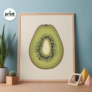Op de afbeelding: Een ingelijste print met een dwarsdoorsnede van een kiwi. De afbeelding toont een groen interieur met zwarte zaden en een lichtgekleurd centrum. De print staat tegen een crèmekleurige achtergrond en is ingelijst in natuurlijk hout. De print is gelabeld met de tekst "print by Marcus Brown".
