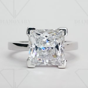 May include: A silver ring with a square-shaped, clear princess-cut diamond.