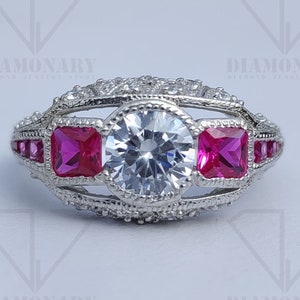 May include: A silver ring with a large round clear stone surrounded by smaller clear stones. The ring has three square pink stones on either side of the large stone.