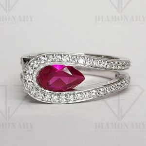 May include: A silver ring with a pear-shaped ruby gemstone surrounded by smaller white gemstones.