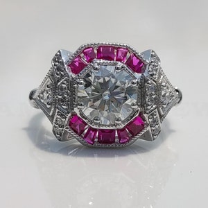 May include: A silver ring with a large round diamond surrounded by a halo of pink square-shaped gemstones.