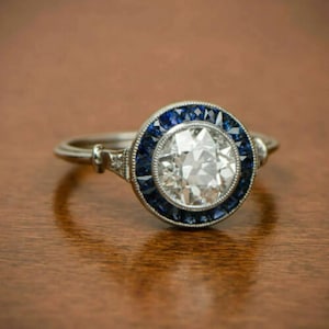 May include: A silver ring with a large round diamond surrounded by a halo of blue sapphires.