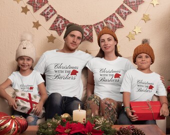 May include: A set of four white short-sleeved t-shirts featuring the black printed text "Christmas WITH THE Barkers" with a small red Santa hat icon above the word Barkers. The shirts are worn by two adults and two children.