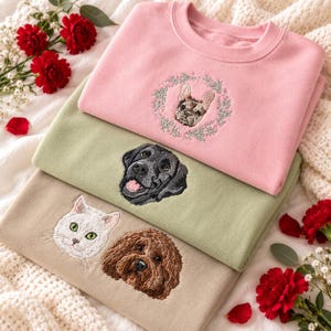 Puede incluir: Tres sudaderas de cuello redondo en rosa, verde salvia y beige. La sudadera rosa presenta un bulldog francés bordado dentro de una corona floral. La sudadera verde salvia tiene un bordado de labrador negro. La beige muestra un gato blanco y un perro marrón de pelo rizado.