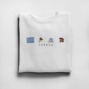 Op de afbeelding: Witte crewneck sweatshirt met een grafisch ontwerp met de Griekse vlag, een gyros, een blauw-wit gebouw en een rood-gouden helm. De tekst "GREECE" is onder de grafiek gedrukt.