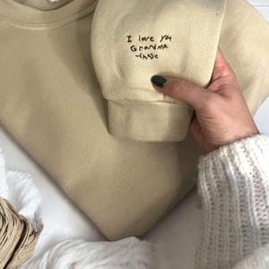 May include: A beige sweatshirt with the text "I love you Grandma -Chase" embroidered on the sleeve.