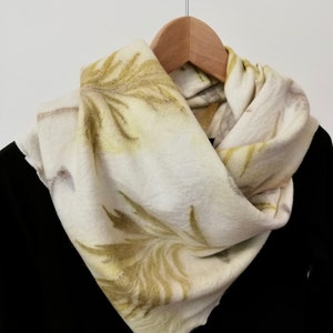 Peut inclure: Une écharpe blanche avec un motif floral vert et jaune. L'écharpe est suspendue à un cintre en bois.