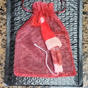 May include: A red and white knitted elf doll with googly eyes, packaged in a red mesh bag with a red ribbon.