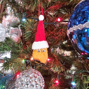 May include: A Christmas tree decorated with ornaments, lights, and a knitted Santa hat with a googly-eyed chicken nugget hanging from it.