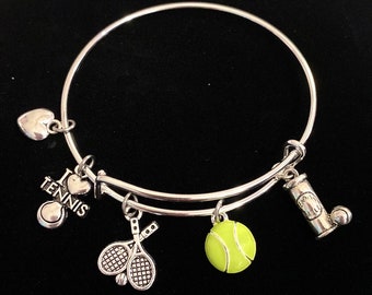 May include: A silver charm bracelet with tennis-themed charms, including a tennis ball, two tennis rackets, a heart with "I love tennis" written on it, and a tennis ball can.